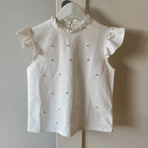 Vit blus 💕 - Jättesöt vit blus med volangärmar och pärldetaljer 🫶🏼Ganska liten i storleken. Obs lappar är avklippta!! 💕Säljer då den är för liten för mig 