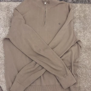Beige half zip tröja från Morris - Snygg beige tröja från Morris med half zip och diskret logga på bröstet. Tillverkad i 100% pima bomull för en mjuk och skön känsla. Långärmad modell med ribbade muddar och hög krage, perfekt för lager-på-lager under hösten och våren. 9/10 knappt använd.