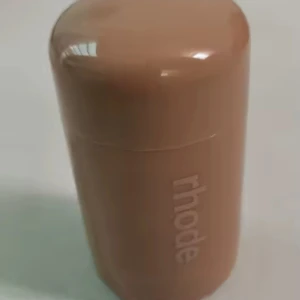 Rhode rouge stick i peach - Krämrouge i stickformat från Rhode i en snygg peach-rosa nyans. Kommer i en beige, rund plastförpackning med lock. Perfekt för att ge kinderna en fräsch glow och enkel att ta med i väskan.