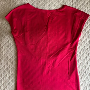 Röd topp med öppen rygg - Säljer en snygg röd topp i stretchigt bomullsmaterial. Toppen har korta ärmar och en djup, öppen rygg som ger en cool och trendig look. Perfekt att styla med jeans eller kjol för en färgstark outfit.