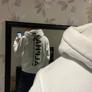 Alpha industries hoodie vit/camo - Alpha Industries hoodie med svart camoflauge logga på ryggen. Lite slitage vid snörningen samt fläck på magen. Annars bra skick.                                     Storlek L men passar mig som vanligtvis har M/S