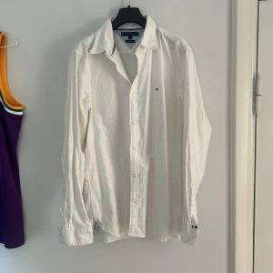 Vit slim fit skjorta Tommy Hilfiger L - Vit skjorta från Tommy Hilfiger i storlek L med slim fit-passform. Klassisk design med knappar framtill, lång ärm och liten broderad logga på bröstet. Skjortan är tillverkad i bomull.