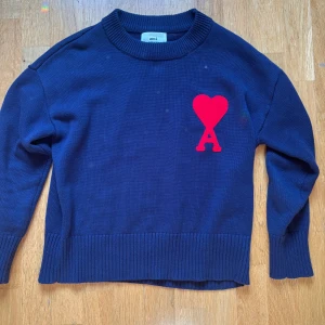 Mörkblå stickad tröja från Ami Paris - Säljer en mörkblå stickad tröja från Ami Paris med ett stort rött hjärta och bokstaven A på bröstet. Tröjan har rund hals, långa ärmar och breda ribbade muddar vid ärmslut och nederkant. Perfekt för dig som gillar stilrena plagg med en twist.