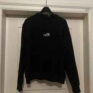 Svart sweatshirt Dsquared2 ICON L - Svart sweatshirt från Dsquared2 i storlek L med vit 'ICON'-text på bröstet. Klassisk rund halsringning och långa ärmar. Tröjan har en clean look och är tillverkad i mjuk bomull, perfekt för dig som gillar stilrena streetwear-plagg. Använd en gång men var för liten i storleken. Hör  gärna av dig om du är intresserad!☺️