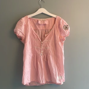 Rosa blus Odd Molly Amor Top - Supersöt ljusrosa blus från Odd Molly, modell Amor Top. Blusen har korta puffärmar med broderad Odd Molly-logga, v-ringning med knappar och fina spetsdetaljer längs halsringningen. Tillverkad i mjuk bomull och har dekorativa veck framtill. Använd ett fåtal gånger och inga defekter💗 xs/s