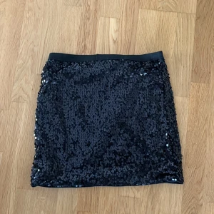 Svart paljettkjol från Lindex  - Snygg svart kortkjol från Lindex, täckt med glittrande paljetter som ger en riktigt festlig vibe. Kjolen har en rak passform och elastisk midja för extra komfort. Perfekt för dig som vill glänsa lite extra!🌸🎉