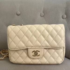 Beige quiltad axelväska i nyskick - Ren, fräsch quiltat skinn väska med guldfärgade detaljer. Väskan har kedjerem och ett fack med dragkedja inuti. Liten storlek, perfekt för det essentiella. 