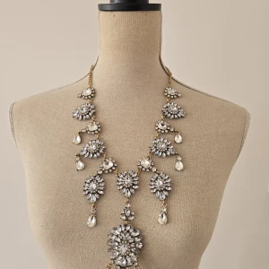 Glittrigt statementhalsband med kristaller - Superfint halsband med stora, glittriga kristaller i silverfärg och droppformade hängen. Kedjan är guldfärgad och smycket har en riktigt lyxig och iögonfallande design som ger wow-effekt till vilken outfit som helst.