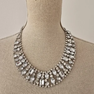 Glittrigt statement halsband i silver - Supersnyggt statement halsband med stora, glittrande stenar i olika former och storlekar. Halsbandet är i silverfärg och ger en lyxig känsla med sina gnistrande detaljer. Perfekt för att lyfta vilken outfit som helst.