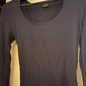 Mörkblå långärmad topp Gina Tricot - Enkel och stilren mörkblå långärmad topp från Gina Tricot. Modellen har rundad urringning och är figurnära i passformen. Perfekt att matcha med jeans eller kjol. Tillverkad i mjuk bomull som känns skön mot huden. Använd ett fåtal gånger. 