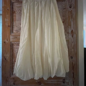 Ljusvit långkjol - Säljer en superfin ljusvit långkjol med voluminös och flowy känsla. Kjolen har resår i midjan och ett skirt, glansigt tyg som ger en elegant look. 