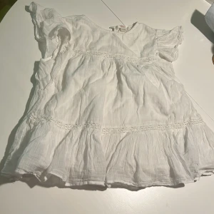 Vit blus med volang från Gina Tricot - Supersöt vit blus från Gina Tricot med volangdetaljer och korta ärmar. Blusen har en luftig och lätt struktur, dekorativa sömmar och en liten knapp i nacken. Perfekt för en fräsch och somrig look!