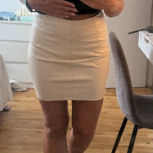 Beige tight kortkjol i syntet - Snygg beige kortkjol med tight passform och stilren look. Kjolen har diskreta sömmar framtill och är perfekt för dig som gillar minimalistisk stil. Materialet känns mjukt och följsamt mot kroppen.