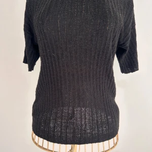 Svart ribbad stickad T-shirt  - Svart stickad t-shirt med ribbat mönster och korta ärmar. Tröjan har rund halsringning och är i ett mjukt, stretchigt material som känns skönt mot huden. Perfekt för lager-på-lager och funkar året runt. Enkel och stilren design som passar till allt. Stl  S