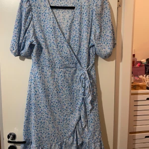 Klänning - Supersöt kort omlottklänning med ljusblått och vitt blommönster. Perfekt för sommaren. 