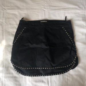 Svart kortkjol med nitar från Hunkydory - Svart kortkjol från Hunkydory med coola silvriga nitar längs kanterna och nedtill. Lite stretchig, men ganska groft material.