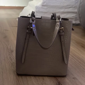 Beige axelväska i crocopräglat skinn Zara - Snygg beige axelväska från Zara i crocopräglat syntetskinn. Väskan har justerbara axelremmar med guldfärgade spännen och ett rymligt fack med dragkedja och tryckknapp. Perfekt för dig som vill ha en stilren och trendig väska med struktur. Så fin och rymlig!❤️