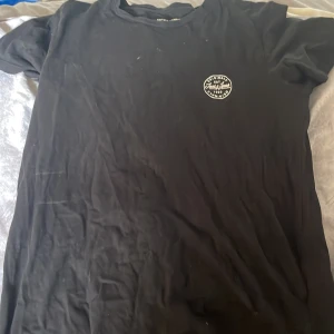 Svart t-shirt från Jack & Jones - Svart t-shirt från Jack & Jones Originals med rund hals och liten vit logga på bröstet. Klassisk passform och tillverkad i mjuk bomull, perfekt till jeans eller shorts. Enkel och stilren design som funkar året runt.