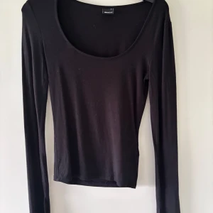 Svart långärmad topp Gina Tricot XS - En svart långärmad topp från Gina Tricot i storlek XS. Toppen har en djup rundad urringning och är figurnära i modellen. Perfekt att styla med jeans eller kjol för en clean och enkel look.