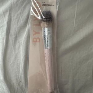 BY LYKO foundation & concealerborste - Dual foundation- och concealerborste från BY LYKO med mjuka syntetiska borst, silverfärgat fäste och ljusrosa handtag. Perfekt för att applicera både foundation och concealer med precision och jämnt resultat.