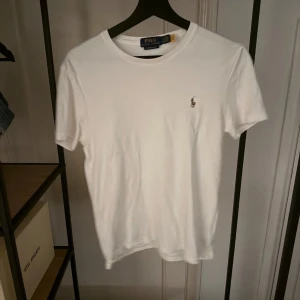 Vit t-shirt från Polo Ralph Lauren - Säljer en klassisk vit t-shirt från Polo Ralph Lauren i custom slim fit. Den har en liten broderad logga på bröstet och är i mycket bra skick. Perfekt för både vardag och fest! 👕✨