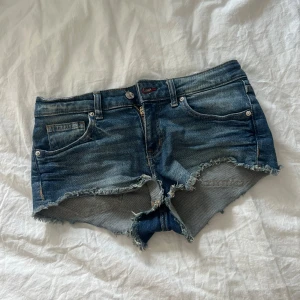 Mörkblå jeansshorts med fransig kant - Snygga mörkblå jeansshorts med rå, fransig kant och klassisk femficksdesign. Lågmidjade och i stretchigt denim som sitter tajt. Perfekta för varma sommardagar och ger en avslappnad vibe.