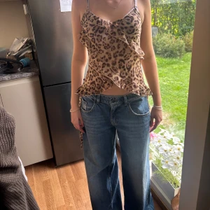 Leopardmönstrad omlottopp med volang - Säljer en leopardmönstrad omlottopp med tunna axelband och volangdetaljer. Toppen har knyt i sidorna och är croppad med en snygg v-ringning. Perfekt för dig som vill sticka ut med ett djurmönster och coola detaljer.