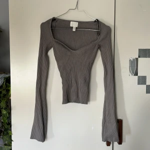 Grå ribbad långärmad topp från H&M - Säljer en grå ribbad långärmad topp från H&M med snygg v-ringning och figurnära passform. Toppen har en modern design med markerade sömmar och är perfekt att styla till olika outfits.