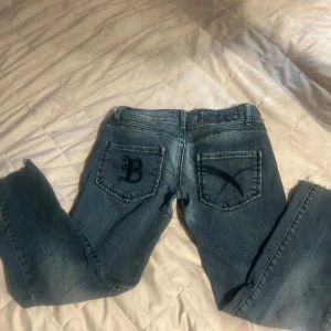 Blå jeansbyxor från Bik Bok med broderad bakficka - Säljer ett par blå jeansbyxor från Bik Bok i storlek M. Byxorna har en normal passform förutom att benen är lite korta och snygga broderade detaljer på bakfickorna, varav ena har ett B. 