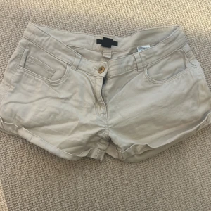 Beige shorts från H&M - Snygga beige shorts från H&M med klassisk femficksdesign och knappstängning. Perfekta för varma dagar och enkla att matcha med olika toppar. Gjorda i mjuk bomull för en bekväm känsla.
