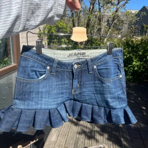 Volangkjol i jeans - Kort jeanskjol med en volang, längd bak 33cm, längd fram: 25cm och midjemått i knapphöjd: 40cm 🫶 skriv vid frågor eller fler bilder🥰