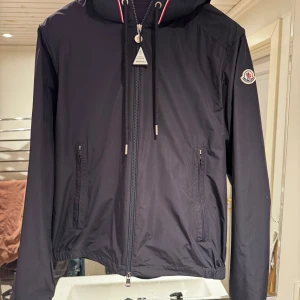 Moncler Mira Hooded Jacket Navy - Riktigt fräsch och fin Moncler windbreaker i navy blå, inte använd så vidare mycket, köpt för 6650kr på CareOfCarl, har orderbekräftelse, storlek 3-L, skriv om du undrar något!