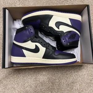 Nike Air Jordan 1 Retro High Court Purple - Säljer ett par Nike Air Jordan 1 Retro High i färgen Court Purple. Skorna har svart, vit och lila läder, klassisk hög siluett och svart swoosh. Perfekta för dig som gillar sneakers med ikonisk design och cool färgkombo. Ny pris 3500kr