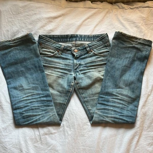 Blå bootcut jeans från wrangler - Säljer ett par skitsnygga klassiska blå wrangler jeans med bootcut passform och låg midja. Jeansen har fem fickor, knappgylf och små slitningar mellan benen och vid fötterna. Perfekta för dig som gillar en tidlös denimlook. Midjemått: 37-38. Innerbenslängd: ungefär 73.  Skriv till mig om du vill ha fler bilder eller övriga frågor! Säljer de pga att de har blivit för små!💕