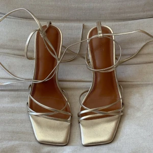 Guldiga klackar med snörning - Säljer ett par helt nya och oanvända, eleganta klackar i guld med smala remmar och snörning. Skorna har fyrkantig tå och klack, vilket ger en trendig look. Säljer p.g.a. passade inte till den klänning jag ska ha. De är från NAKD och nypris är 600kr. Skickar i orginalfärpackning. Storlek 38.