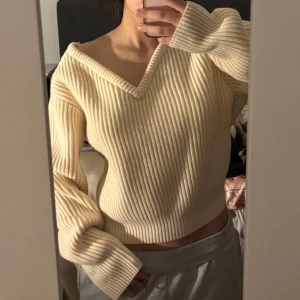 Ribbad offwhite croppad tröja - Säljer en ribbad offwhite tröja med v-ringning och croppad passform. Tröjan har långa ärmar och är tillverkad i ett mjukt stickat material. Perfekt för lager-på-lager och enkel att matcha med olika outfits.