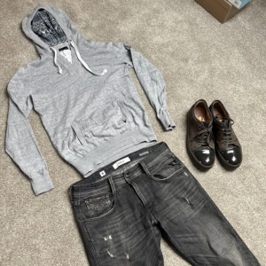 Grå hoodie från Farah - Säljer en stilren grå hoodie från Farah med justerbar huva och magficka. Tröjan har långa ärmar och ribbade muddar  Storlek S, köp för endast 299.