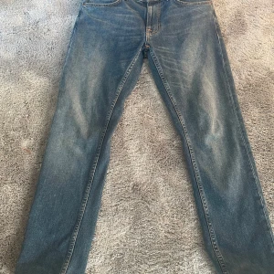 Blå jeans från Nudie Jeans - Säljer ett par klassiska blå jeans från Nudie Jeans modell lean Dean (slim fit). Jeansen har en enkel design utan extra detaljer och är tillverkade i denim med lätt tvättad look. Perfekta för en avslappnad stil. Använda typ 3 gånger dom är förstora för mig i midjan. Storlek 32/30