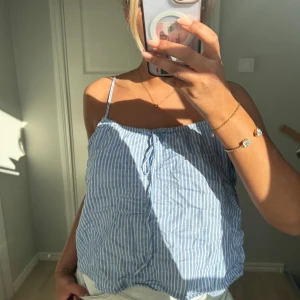 Randig och vit linnetopp med tunna axelband - Säljer nu två olika linnetoppar med tunna axelband. Ena är blå- och vitrandig med knyt fram, andra är helvit med samma knyt-detalj. Båda har lös passform och är perfekta för varma dagar. 350 kr för båda två. Storlek s. Från H&M💕