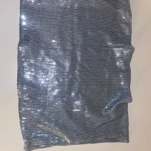 Silver paljetttopp från COLLUSION - Säljer en glittrig silverfärgad kjol från COLLUSION, täckt med små paljetter som ger ett riktigt snyggt skimmer. Toppen är rak i modellen och har en kort längd, perfekt för att sticka ut. Säljer för att den användes på en tema fest men kom alldrig till användning efteråt 