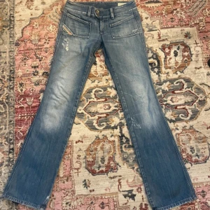 Blå bootcut jeans från Diesel - Säljer ett par blå bootcut jeans från Diesel med slitna detaljer och dubbla knappar i midjan. Midjemått- 36 innerbenslängd - 80 