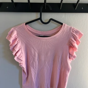 Rosa ribbad topp med volangärmar - Säljer en söt rosa ribbad topp med volangdetaljer på ärmarna. Är i storlek 158/ 164 men jag skulle säga att den även passar både xs och s.🩷