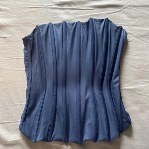 Blå korsettopp från Bershka - Säljer en blå korsettopp från Bershka med markerade sömmar som ger en snygg form. Toppen är ärmlös och har en stilren design som passar perfekt till många olika outfits.