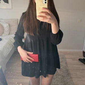Svart volangklänning  - Säljer en svart kortklänning med långärmad design och volangdetaljer. Klänningen har en lös passform och knappar framtill upptill. Det är en gammal klänning från H&M som jag tyvärr säljer pga att den är för kort på mig som är ca 163cm. Superfin och i mycket bra skick!💛💛