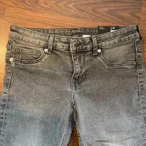 Grå flare jeans med låg midja - Säljer ett par grå jeans med flare-ben och låg midja. Jeansen har klassisk femficksdesign, bälteshällor och silverfärgade knappar. 