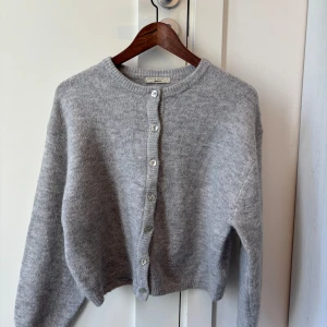 Grå stickad kofta från Gina Tricot - Mysig grå stickad kofta från Gina Tricot med rund halsringning och pärlemorknappar framtill. Perfekt för lager-på-lager och enkel att matcha med olika outfits.