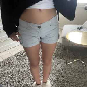 Ljusgråa jeansshorts med knapp - Snygga ljusgråa jeansshorts med klassisk femficksdesign och knapp framtill. Shortsen har låg midja och uppvikta benslut för en avslappnad look. Perfekta för varma dagar och enkel att matcha med olika toppar.