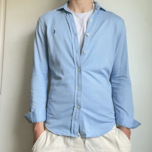 Ljusblå skjorta från Polo Ralph Lauren - Säljer en ljusblå skjorta från Polo Ralph Lauren i slim fit-modell. Som aldrig är använd! Skjortan har klassisk krage, knappar framtill och broderad logga på bröstet. Perfekt för dig som gillar stilrena och tidlösa plagg. Skriv vid funderingar eller frågor!