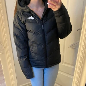 Svart pufferjacka från Nike - Säljer en svart pufferjacka från Nike med huva och dragkedja framtill. Det är barnstorlek men är större typ av jacka. Använd 2-3 gånger🩷
