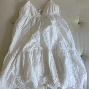 Vit sommarklänning med broderade detaljer från Zara - Supersöt vit klänning från Zara med tunna axelband och broderade blommor. Klänningen har v-ringning, knyt i ryggen och volang nertill. Den är köpt på Zara för några år sedan och säljs inte längre. Den är lite ihop syd i v ringningen och det finns bild på de i bilderna. 